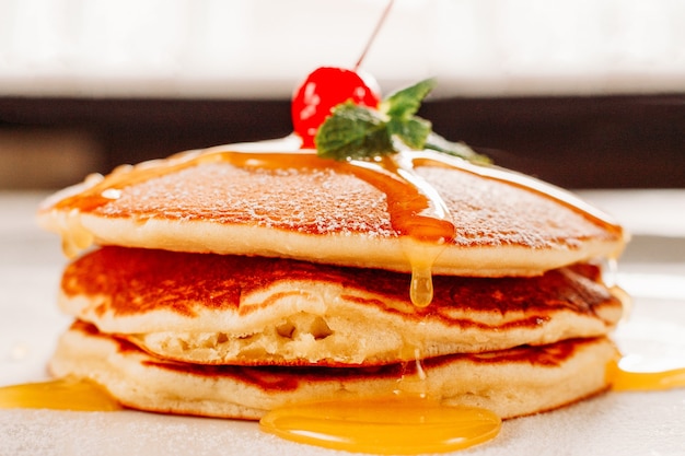 les crêpes aux crêpes s'empilent avec la cerise en poudre de sucre sur le dessus.