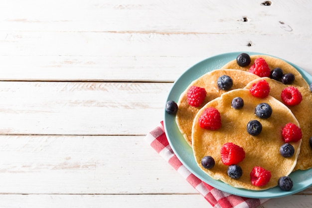 Crêpes aux framboises, bleuets et miel sur table en bois blanc Copyspace