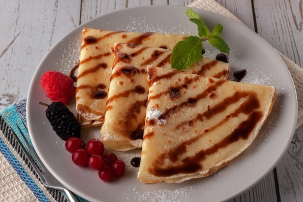 Crêpes aux framboises, groseilles et chocolat sur une assiette, décorées d'une feuille de menthe