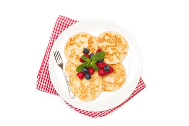 Crêpes aux framboises et myrtilles sur une plaque blanche et sur fond blanc en vue de dessus