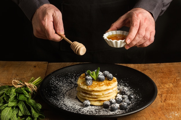 Crêpes aux myrtilles sur une plaque noire et un homme avec une louche de miel