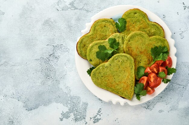 Crêpes d'avocat aux épinards en forme de coeur avec sauce au yaourt grec et tomates cerises sur plaque blanche sur fond gris clair. Concept de nourriture pour le petit-déjeuner. Vue de dessus avec espace de copie.