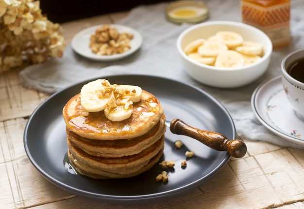 Crêpes à la banane, aux noix et au miel, servies avec du thé. Style rustique.