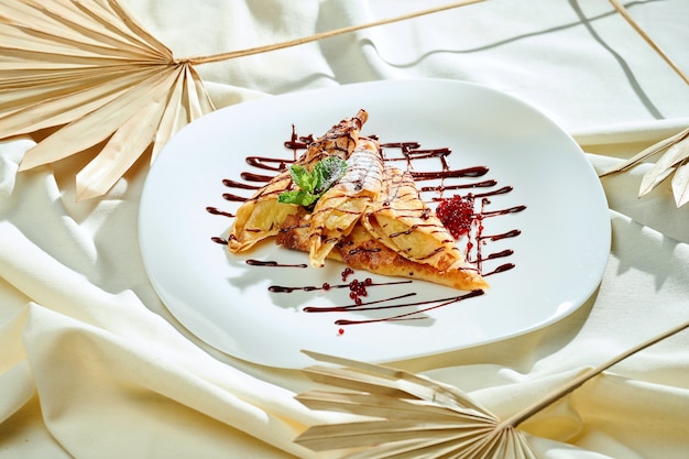 Photo crêpes à la banane, caramel, chocolat dans une assiette blanche sur une feuille. crêpes françaises