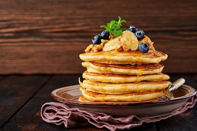 Crêpes à la banane, noix, miel et caramel pour un petit déjeuner sur fond de bois foncé. Mise au point sélective.