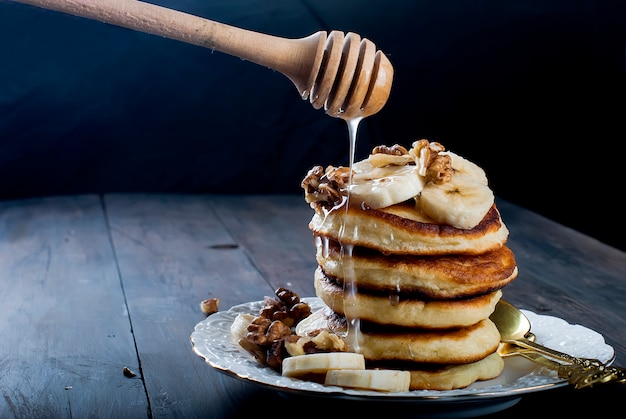 Crêpes à la banane, noix, miel et verre de café sur fond noir