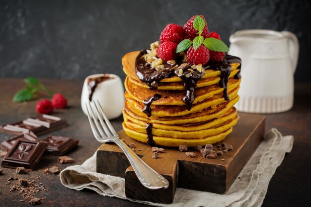 Crêpes à la citrouille avec framboises fraîches, chocolat et noix sur pierre foncée ou béton.