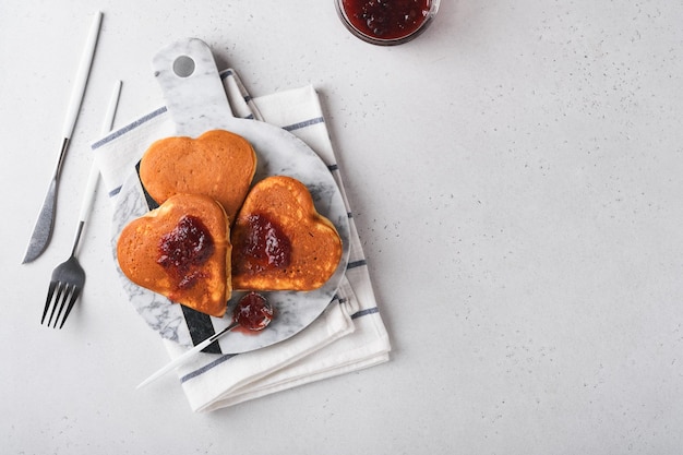 Crêpes Avec Confiture De Baies Et Miel En Forme De Coeur Et Tasse De Café Chaud Sur Fond De Bois Blanc. Concept De Petit-déjeuner Pour La Saint Valentin Ou Agréable Surprise Pour Un être Cher Table Vue Du Dessus