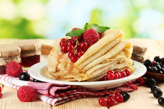 Crêpes avec confiture de baies et miel sur table en bois sur fond vert