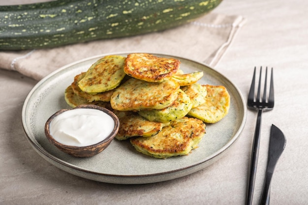 Crêpes de courgettes végétariennes aux légumes avec crème sure sur une assiette ronde et courgettes vertes