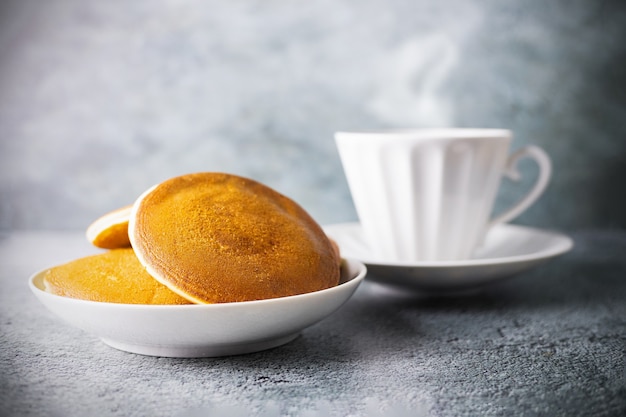 Crêpes dans un plat et tasse de thé ou de café floue avec de la vapeur et de la porcelaine sur une surface grise