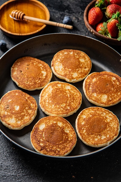 Crêpes dans une poêle avec des baies fraîches et du miel