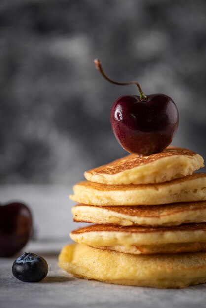 Crêpes empilées aux cerises et aux bleuets sur une table en bois gris vintage Espace réservé au texte