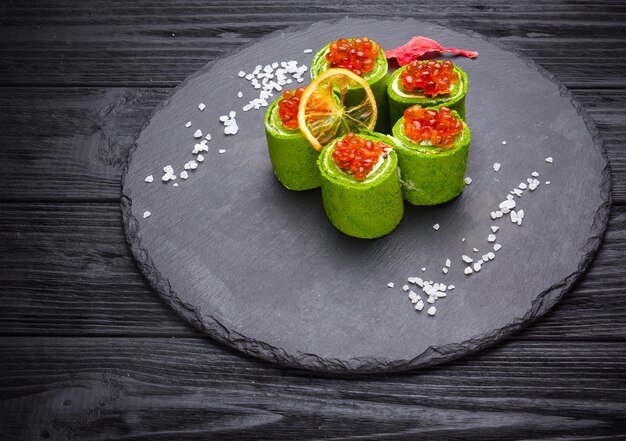 Crêpes d&#39;épinards verts au caviar rouge et fromage à la crème sur fond en bois