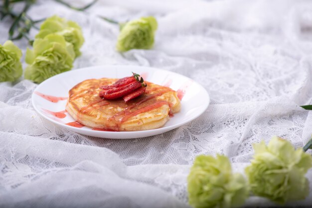 Crêpes faites maison avec des baies et du miel sur une assiette rose sur une surface en bois blanche