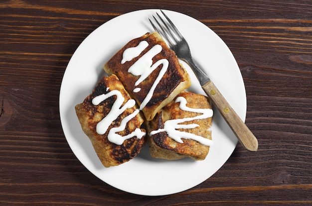 Crêpes faites maison avec de la viande et de la crème sure sur une table en bois foncé, vue de dessus