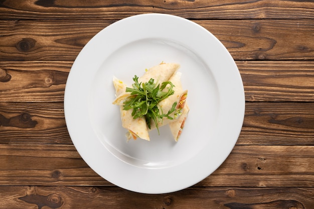 Crêpes farcies au saumon, fromage à la crème, laitue et roquette dans une assiette en céramique blanche sur une table de cuisine en bois