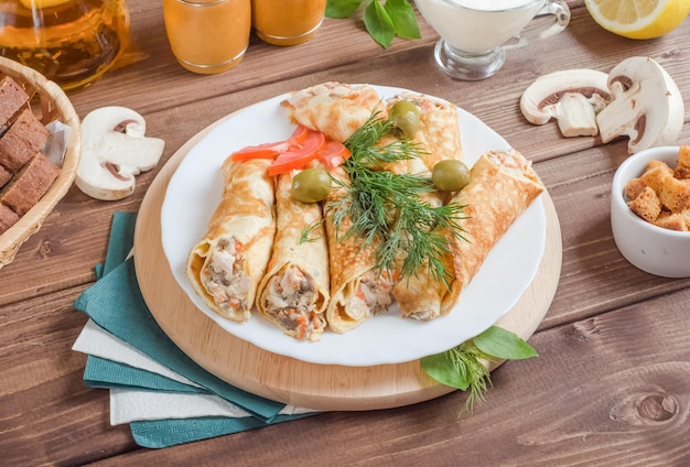 Crêpes farcies farcies au fromage et champignons décorés d'herbes sur une plaque blanche sur un fond en bois