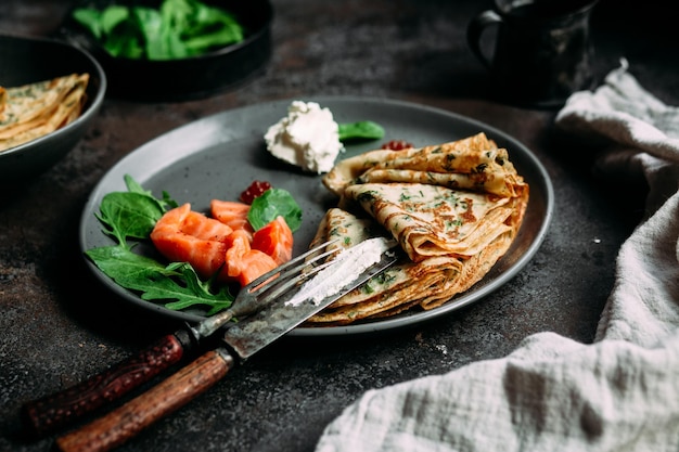 Crêpes fines aux herbes, saumon et fromage à la crème sur une assiette