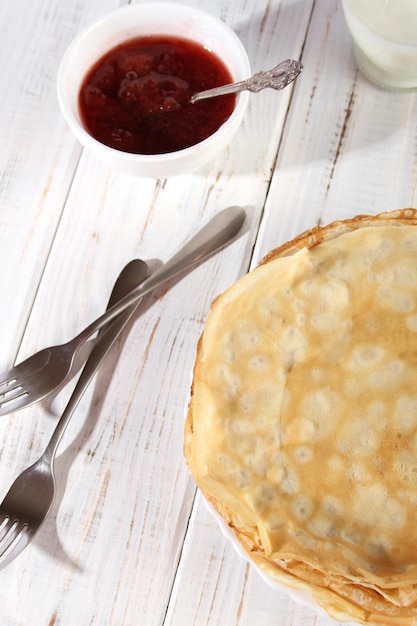 Crêpes fines et chaudes avec de la confiture de fraises sur une table en bois blanche Holiday Maslenitsa