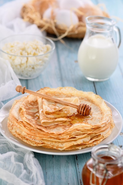 Crêpes fines faites maison avec du miel empilées dans une pile sur une table avec un pot de lait