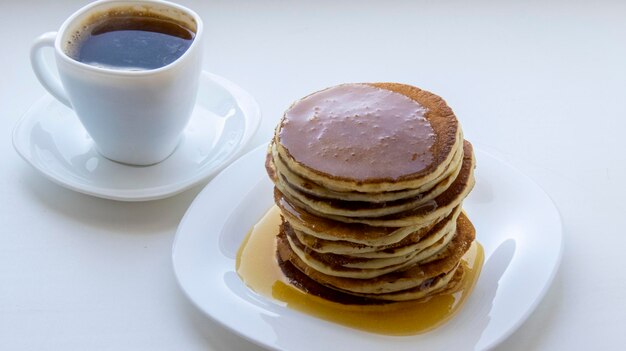 Crêpes sur un fond blanc versé avec du miel gros plan des crêpes saupoudrées de miel prêt pour le petit déjeuner sur une plaque blanche avec une tasse de café