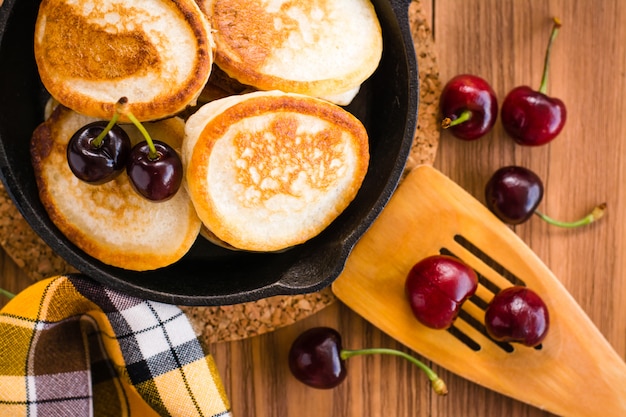 Crêpes Frites Dans Une Poêle En Fer Et Des Cerises Mûres Sur Une Table En Bois. Vue De Dessus