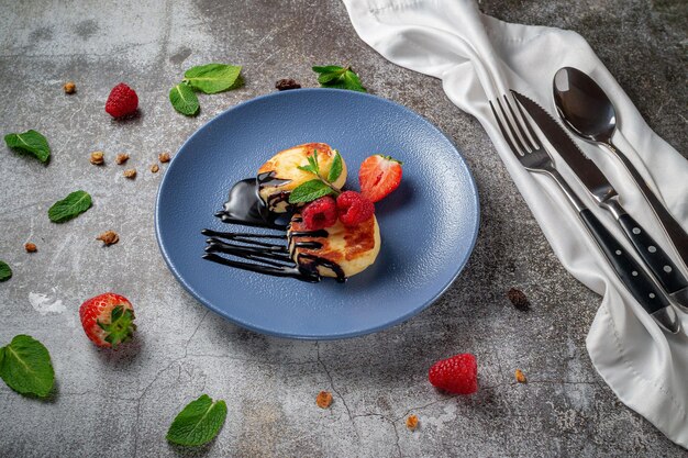 Crêpes frites avec sirop de chocolat et framboises et menthe dans une assiette bleue contre une table en pierre grise. Un petit déjeuner sucré le matin