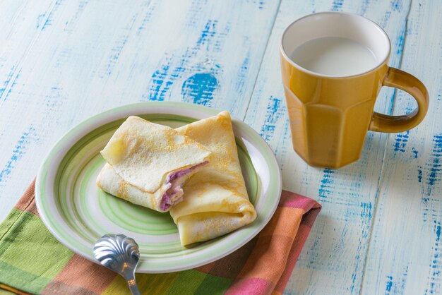 Crêpes maison avec une garniture et une tasse de lait sur un fond en bois