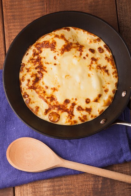 Crêpes maison sur une poêle avec cuillère en bois crème sur table en bois