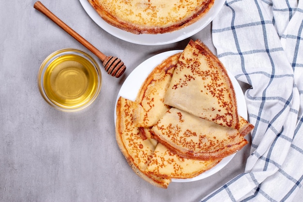 Crêpes minces sur une assiette blanche avec du miel. Vue de dessus.