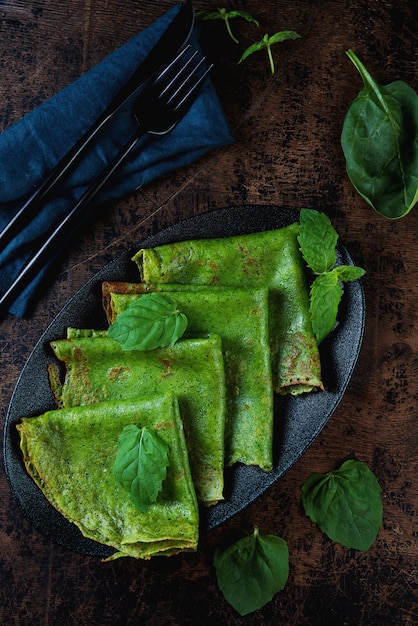 Les crêpes minces aux épinards sont vertes sur une table en bois. Photo verticale. Vue de dessus