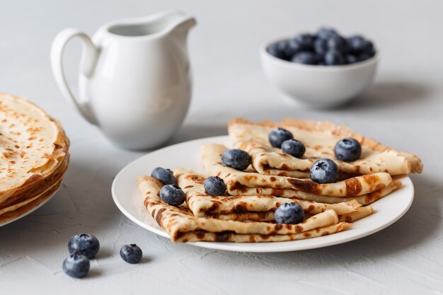 Crêpes minces sur plaque blanche avec des bleuets et de la crème sure. Fermer.