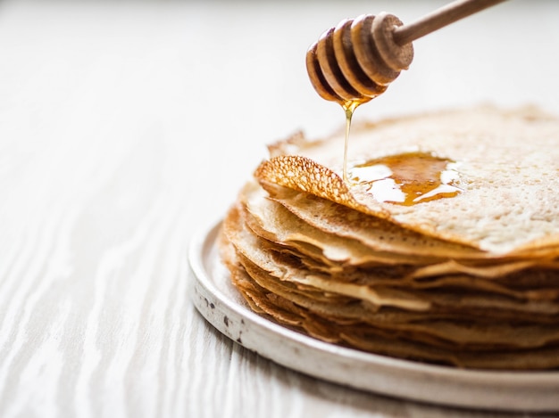 crêpes minces sur plaque blanche et le miel coule d'une cuillère en bois