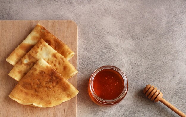 Crêpes minces pliées en triangles avec du miel sur fond gris