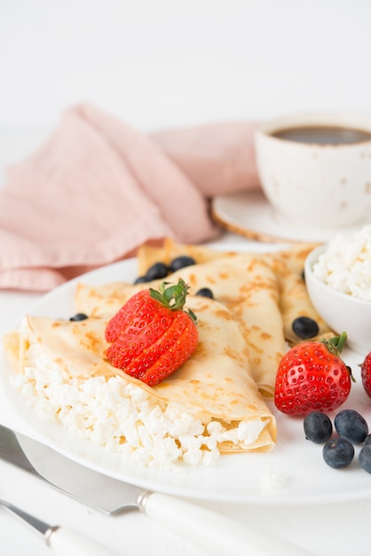 Photo crêpes minces russes traditionnelles avec du fromage cottage et des baies dans une assiette sur un fond blanc