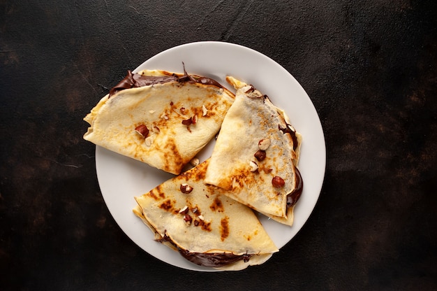 Crêpes à la pâte de chocolat et aux noisettes, sur une plaque blanche sur fond de béton, ardoise