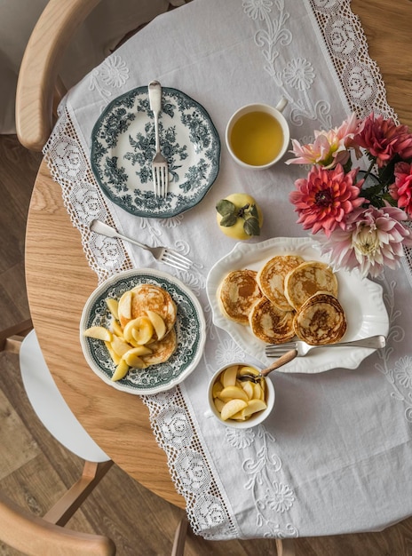 Crêpes de petit-déjeuner maison confortables avec compote de pommes sur des plats vintage un bouquet de thé vert asters sur une table en bois vue sur le dessus