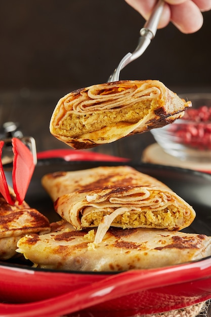 Crêpes avec des piqûres de viande sur une fourchette sur un fond en bois foncé.