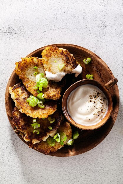 Crêpes de pommes de terre au yaourt et oignons verts et poivre noir dans des pots en argile sur fond blanc