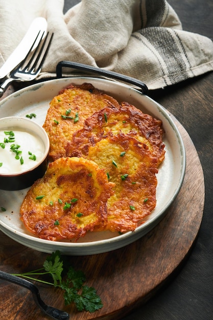 Crêpes de pommes de terre Crêpes de pommes de terre maison frites ou latkes avec crème et oignons verts dans une assiette rustique sur fond de table en bois noir ancien Style rustique Alimentation saine Vue de dessus