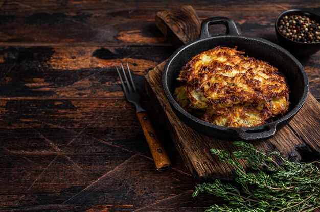 Crêpes de pommes de terre frites ou beignets aux herbes dans une casserole. Table en bois foncé. Vue de dessus.