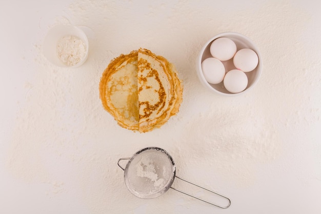 Crêpes rondes minces avec des œufs de poule et de la farine sur une assiette blanche frite