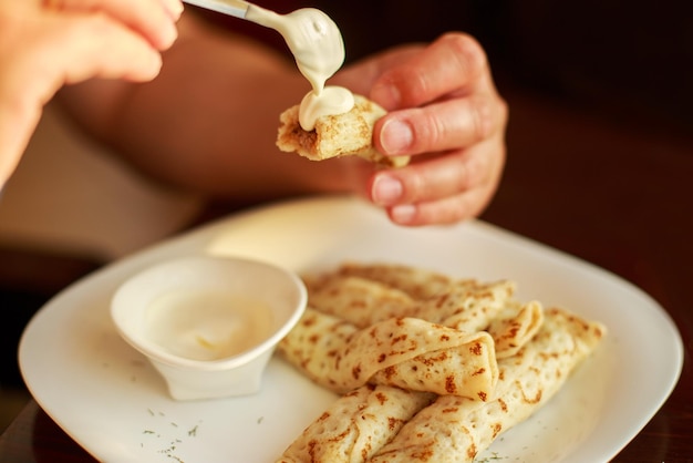 Crêpes roulées dans une paille sur une assiette avec de la crème sure man eating pancake