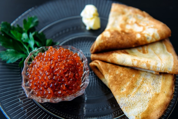 Crêpes russes minces traditionnelles avec caviar rouge, beurre et légumes verts