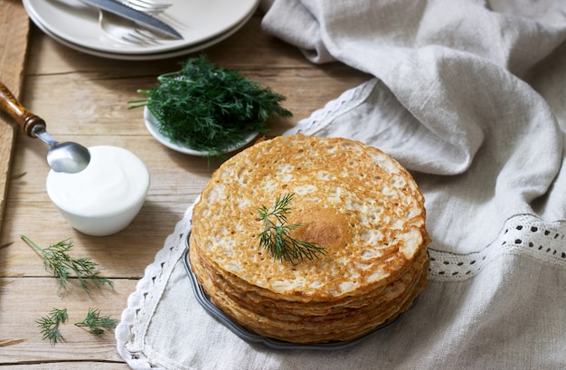 Crêpes de sarrasin servies avec de la crème sure et de l'aneth sur une table en bois. Style rustique.