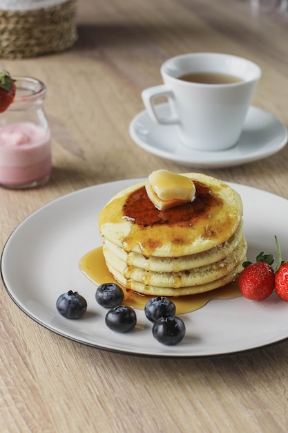 Crêpes servies avec beurre miel et fruirs servis sur une table en bois