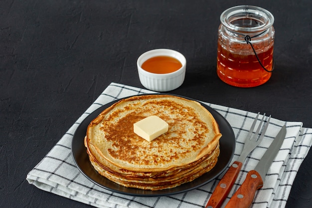 Crêpes servies avec du sirop de miel et du beurre sur une assiette noire. Crêpes traditionnelles pour la semaine des crêpes ou le mardi gras.