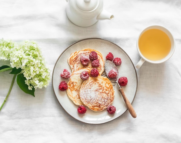 Crêpes simples du matin avec des framboises, du sucre en poudre et du thé vert sur une vue de dessus de fond clair