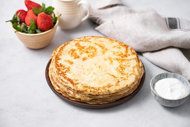 Crêpes sucrées empilées avec de la crème sure et des fraises fraîches sur fond clair Le concept de petit-déjeuner fait maison